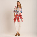 Full-length view of the abstract print blouse paired with off-white trousers, brown loafers and a coral jacket tied at the waist.
