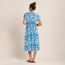 Rear view of a blue and white floral midi dress with short sleeves and elasticated waist, styled with black sandals, shown against a plain studio backdrop.