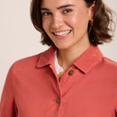 Close-up of coral jacket collar and button fastening, layered over a white blouse, with gold hoop earrings.