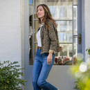 Lifestyle shot of the leopard print jacket worn over a white top and blue jeans, shown outdoors by a doorway.