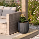 Dark grey ribbed plant pot with flowers beside a rattan garden sofa on a patio