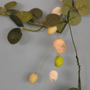 Detailed close-up of the garland with pale green and dark green eucalyptus leaves and hanging speckled eggs in soft yellow, cream, and light green against a pale blue backdrop.