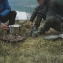 Campers using Easy Camp cooking set on portable gas stove outdoors with pot heating on rocky ground.