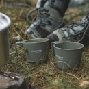 Two green Easy Camp camping cups placed on grass beside hiking boots and stove setup.