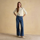 Full-length view of woman wearing striped Breton top with wide leg blue jeans and cream shoes.
