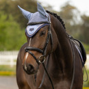 Brown horse wearing a light blue ear bonnet and bridle, standing outdoors. The background is blurred, with green trees and a white fence.