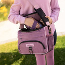 A person in a pink outfit holds a matching lavender LeMieux bag with black straps, standing on a green lawn. The scene conveys a casual and coordinated vibe.