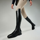 A person wearing beige riding breeches and tall black leather equestrian boots walks confidently against a gray background, conveying elegance and style.