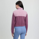 A person with long dark hair is wearing a mauve and pink jacket with text on the collar, paired with light blue leggings. The background is plain gray.