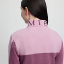 A person with long dark hair, seen from behind, wearing a pink and mauve jacket. The collar has "MI" visible in purple embroidery.