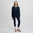 Teen girl in navy sweater with "LeMieux" text and leggings, standing confidently. Wears white socks and beige sneakers. Neutral background.