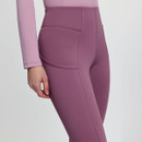 Woman in pink activewear, including a long-sleeve top and leggings, stands smiling. The background is plain gray, conveying a calm, sporty vibe.