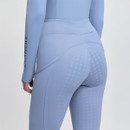 A person wearing light blue equestrian leggings with white grip patterns stands in profile. The word "LeMieux" is printed on the sleeve.