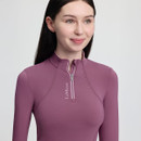 Young woman in a mauve zip-up top, smiling softly. The top has "LeMieux" text near the zipper. The background is a plain light colour.