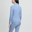 A woman in a light blue fitted athletic outfit stands turned away, showcasing the sleek design. The soft background enhances the outfit's calm tone.