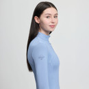 Young woman with long dark hair wearing a light blue LeMieux sports top, looking calmly at the camera, set against a plain white background.