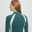 Rear view of a person with long red hair wearing a teal and light yellow athletic top with "LeMieux" on the collar. The setting is minimalist.