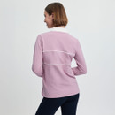 A woman with short hair is seen from behind, wearing a light pink long-sleeve top with white trim and dark pants. The background is a plain, soft grey.