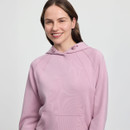 Smiling woman wearing a light pink hoodie with the word “Feminin” subtly embossed on the front. She stands against a plain white background, conveying a relaxed, cheerful vibe.