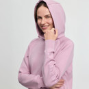 A woman smiles warmly while holding the hood of her light pink hoodie, which has "Le Mieux" embossed on the sleeve. The background is plain white.