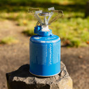 Campingaz compact gas stove on blue butane/propane cartridge placed on a rock outdoors.