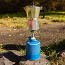 Moka coffee pot brewing on Campingaz portable gas stove set on outdoor ground.