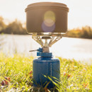 Camping stove with cooking pot on top of Campingaz butane/propane gas canister by a lakeside.