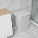 Light grey woven-style laundry hamper with lid closed, positioned in a tiled bathroom next to a shower enclosure.
