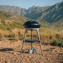 Carri Chef 40 set up outdoors on rocky ground with mountains in the background, connected to small gas canisters beneath the stand.