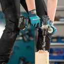 Makita cordless drill with auger bit drilling into wooden post creating wood chips.