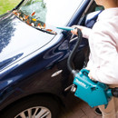 Person using Makita cordless portable vacuum with hose and crevice nozzle to clear leaves from car bonnet near windscreen.