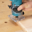 A close-up of a Makita trim router cutting a wood edge.