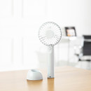 White handheld fan with detachable base shown separately on a desk, highlighting removable stand feature.