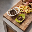 Two kitchen tools, a white cutter and a green apple corer, rest on a wooden surface beside freshly cut potato sticks and whole potatoes in a paper bag.