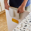 Person attaching a wall-mounted holder to a cupboard door for storing a dustpan and brush set.
