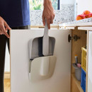 Dustpan and brush set stored neatly inside a cupboard door, with the brush clipped into the pan for compact storage.
