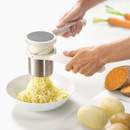 Person using a handheld potato ricer to press cooked potatoes into fine strands over a bowl, with whole and peeled potatoes nearby.