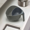 Two nesting grey colanders with handles shown together on a kitchen worktop, demonstrating compact storage.