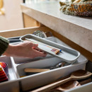 Hand placing a slim tray of chopsticks into an organised cutlery drawer with compartments.