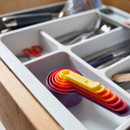 Expandable cutlery tray in a drawer holding utensils, with nested measuring spoons stored neatly.