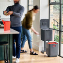 Modern kitchen scene with a person placing food waste into a caddy while another person uses a dual-compartment recycling bin with pull-out lower section.