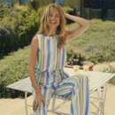 Woman wearing a pastel striped sleeveless top and matching trousers, sitting outdoors in a sunny garden setting.