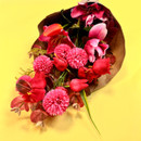 A bouquet of pink and red flowers lying on its side on a bright yellow background, partially unwrapped.