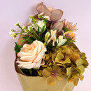 Close-up of a bouquet featuring peach roses, cream blooms and green hydrangea-style flowers in brown paper wrapping.