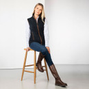 Model seated on a stool wearing the navy fleece gilet, checked shirt, jeans and brown knee-high boots.