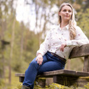 Woman wearing the pheasant print shirt seated outdoors on a wooden bench, styled with jeans in a countryside setting.