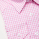 Close-up of a children’s pink and white gingham check shirt showing collar, buttons and chest pocket detail.