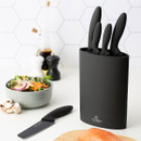 Black knife block set with multiple kitchen knives on countertop, рядом with fresh salad, mushrooms and salmon fillet, modern kitchen setup