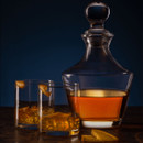 Crystal decanter with whiskey and two old fashioned glasses with ice and orange peel garnish, moody blue background cocktail scene