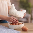 Person placing brown eggs into white ceramic hen-shaped egg storage container, farmhouse kitchen scene with rustic table and striped cloth